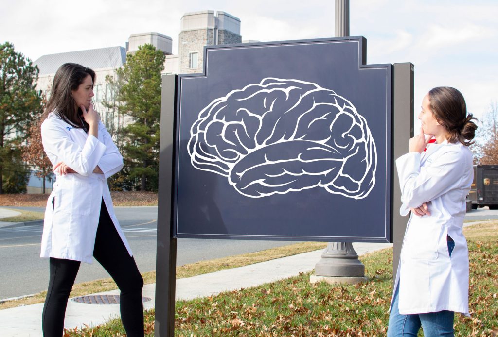 The two students studying the sign, which now has a drawing of a brain on it.